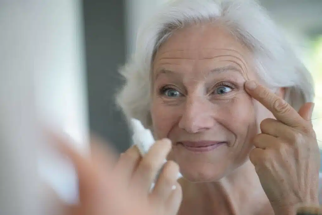 Older woman examining facial lines in mirror, evaluating skincare options beyond Botox for more advanced aging concerns.