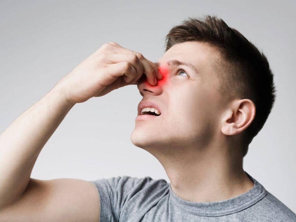 A man holding the bridge of his nose with a red highlighted area indicating pain or a deviated septum, illustrating the functional discomfort associated with a crooked nose.