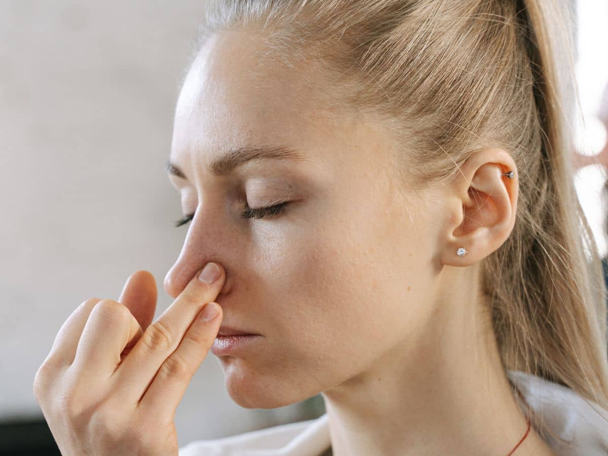 Close-up side profile of a woman with her eyes closed, gently touching the side of her nasal bridge to feel for structural alignment and symmetry.