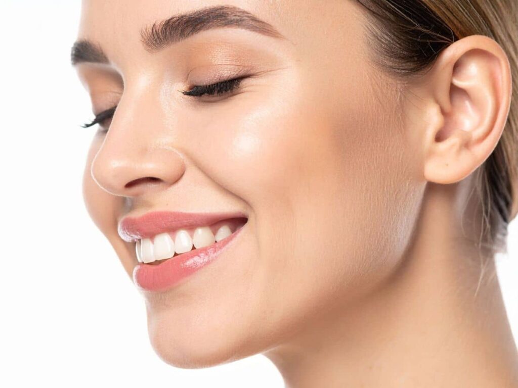 A close-up side profile of a woman smiling with a perfectly straight and symmetrical nasal bridge after corrective rhinoplasty.