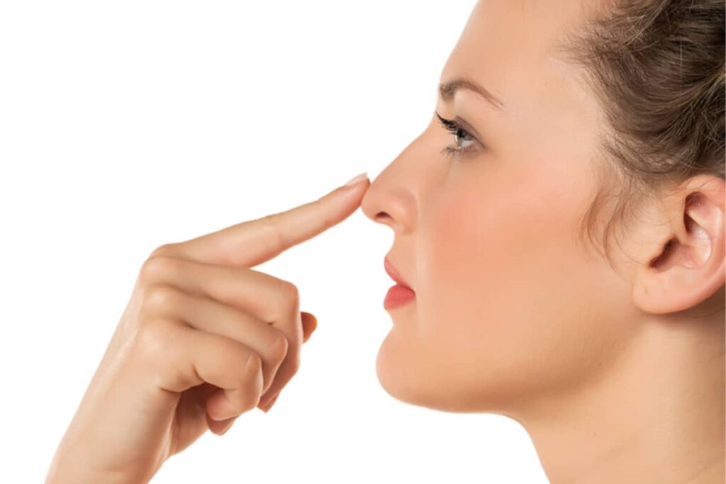 Side profile of a woman pointing to her refined nasal tip and straight bridge after a cosmetic rhinoplasty, showcasing improved facial symmetry and profile balance.