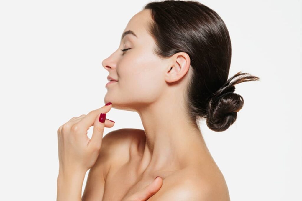 Side profile of a woman touching her chin and admiring her nasal results, showcasing the facial harmony achieved through professional cosmetic rhinoplasty.