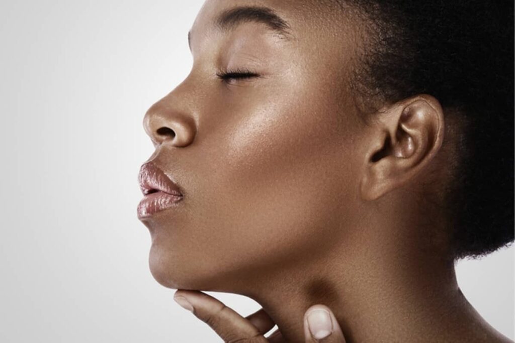 A close-up profile of a Black woman with her eyes closed, highlighting her natural nasal bridge and refined jawline.