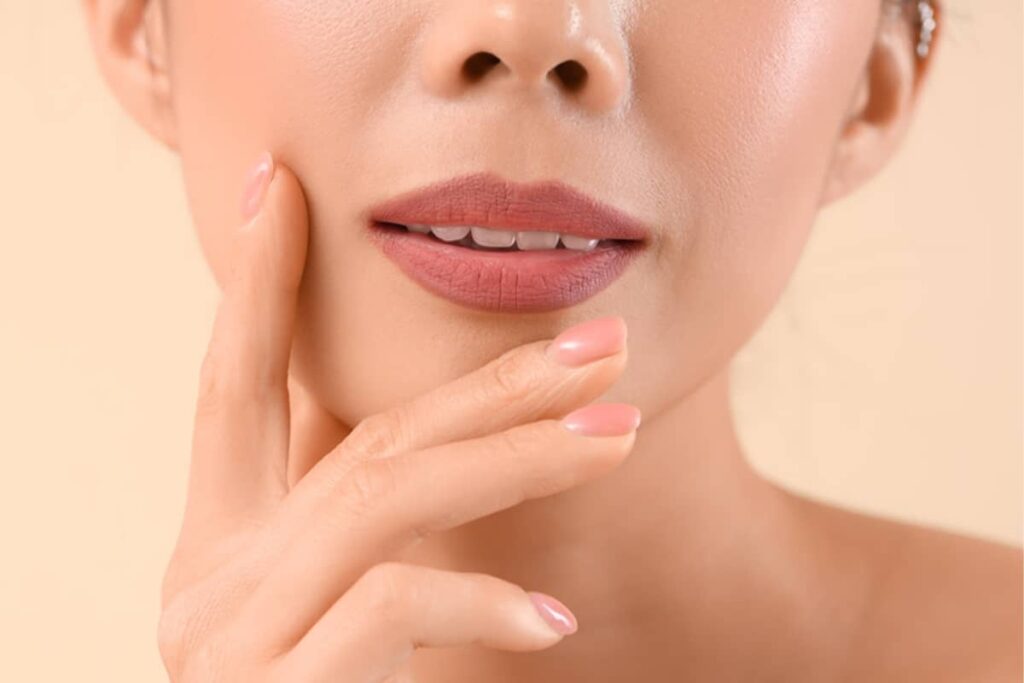 A close-up view of a woman’s lips and lower face, with her hand elegantly placed near her chin to showcase refined lip contours.